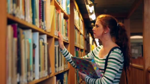 Estudiante enfocado escogiendo un libro en la biblioteca — Vídeos de Stock