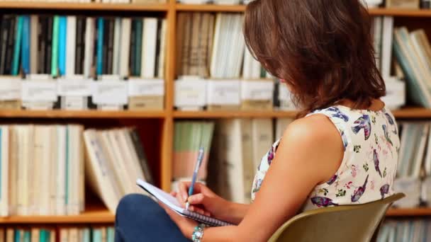 Mujer joven estudiando en la biblioteca con bloc de notas — Vídeo de stock