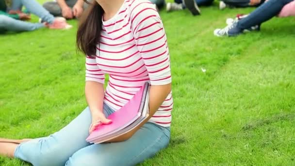 Student med vänner bakom henne på gräset — Stockvideo