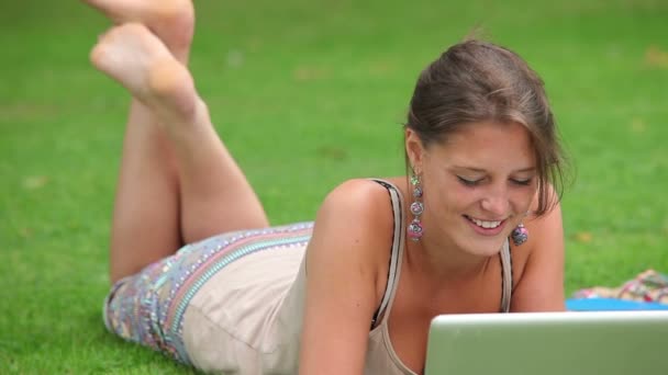 Гарненька студент лежить на траві за допомогою ноутбука — стокове відео