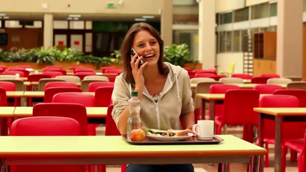 Student answering her phone while having lunch in canteen — Stock Video