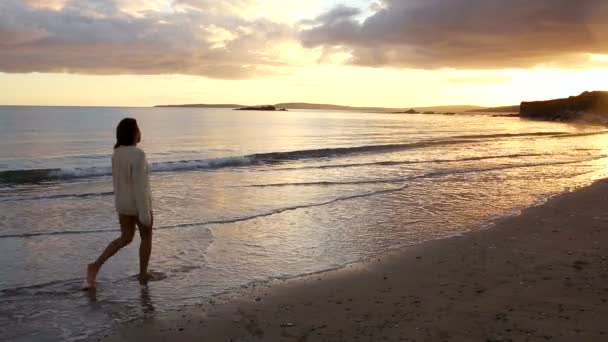 Vrouw slenteren langs het water bij zonsondergang — Stockvideo