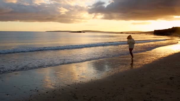 Жінка біжить уздовж води на заході сонця — стокове відео