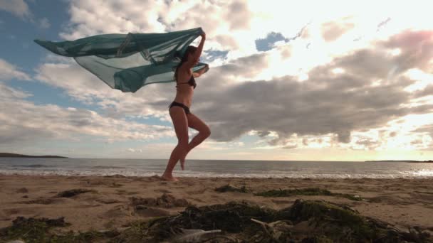 Mujer rebotando en la playa sosteniendo una bufanda — Vídeo de stock