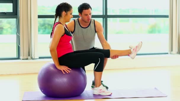 Mujer bonita entrenamiento sentado en la pelota de fitness con entrenador — Vídeo de stock