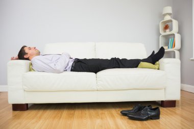 Tired businessman sleeping on sofa in living room clipart
