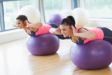 Two fit women stretching out hands on fitness balls in gym clipart