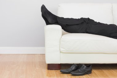 Low section of businessman resting on sofa in living room clipart