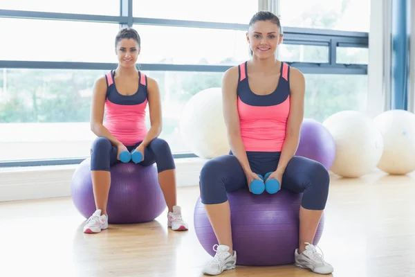 Two fit women with dumbbells on fitness balls in gym — Stock Photo, Image