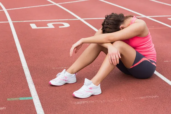 Mujer deportiva tensa sentada en la pista de atletismo — Foto de Stock