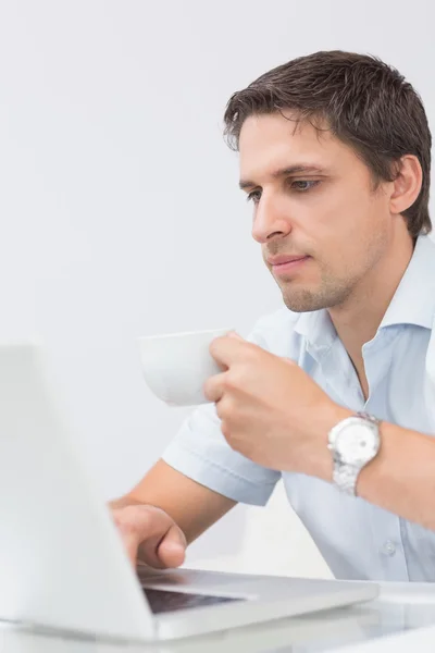 Homem sério com xícara de chá usando laptop em casa — Fotografia de Stock