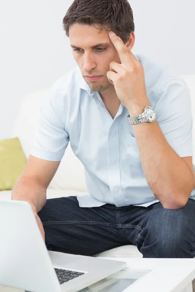 Serious young man using laptop in living room — Stock Photo, Image