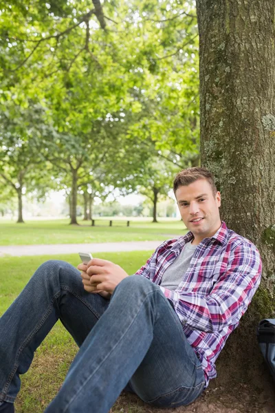 Happy student sending a text outside leaning on tree — Stock Photo, Image