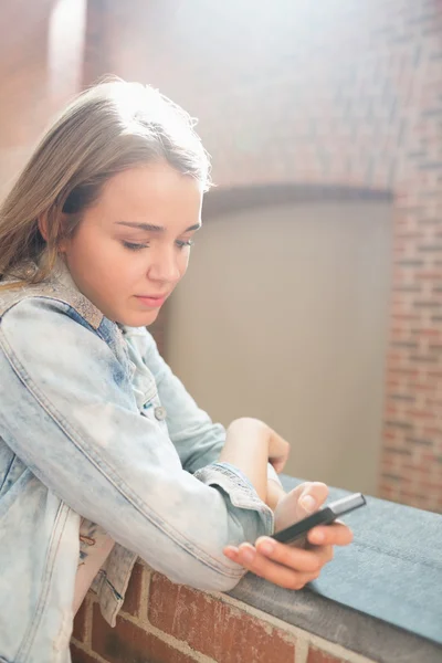 Cheerful student standing in the hall sending a text message — Stock Photo, Image