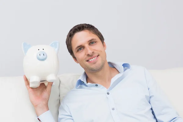 Schöner Mann mit Sparschwein im Wohnzimmer — Stockfoto