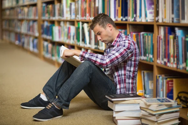 Knappe jonge student zittend op de vloer van de bibliotheek lezen van boek — Stockfoto