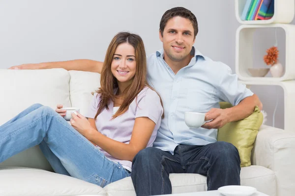 Bonito casal sentado no sofá com xícaras de chá em casa — Fotografia de Stock