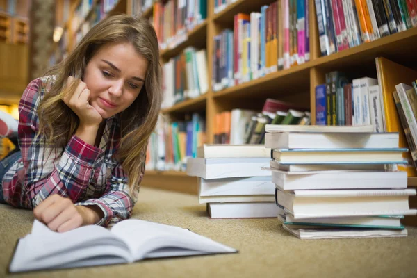 Молодой счастливый студент лежит на полу библиотеки, читая книгу — стоковое фото