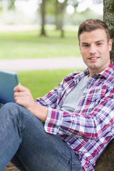 Étudiant joyeux en utilisant sa tablette PC à l'extérieur appuyé sur l'arbre — Photo