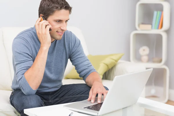 Homem usando celular e laptop na sala de estar — Fotografia de Stock