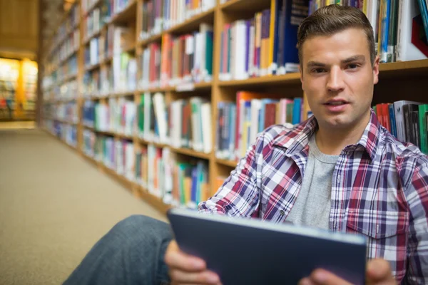 Jovem estudante sentado no chão da biblioteca usando tablet — Fotografia de Stock