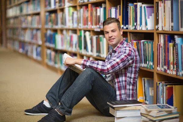 Hübsche junge Studentin sitzt auf dem Boden der Bibliothek und liest Buch — Stockfoto