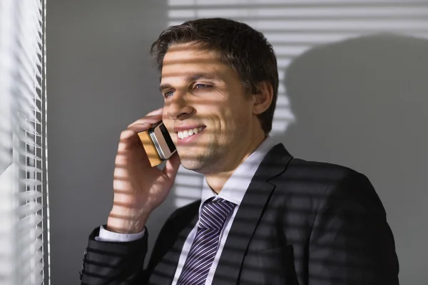 Businessman peeking through blinds while on call in office — Stock Photo, Image