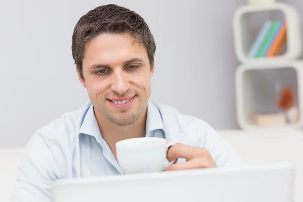 Primer plano de un hombre con taza de té usando el ordenador portátil en casa —  Fotos de Stock