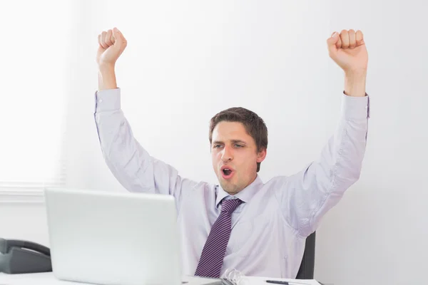 Businessman cheering in front of laptop in office — Stock Photo, Image