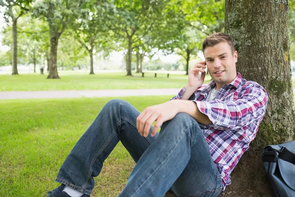 Gelukkig student op de telefoon buiten leunend op boom — Stockfoto