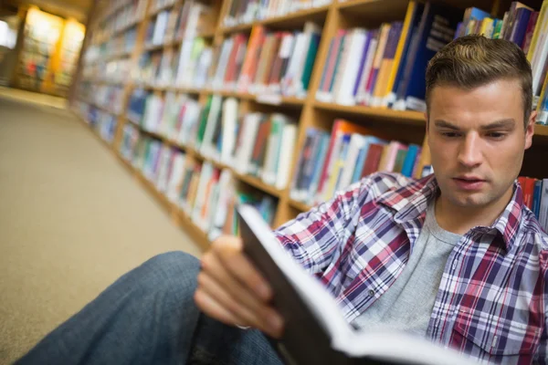 Фокусований молодий студент сидить на бібліотеці читання книг підлоги — стокове фото