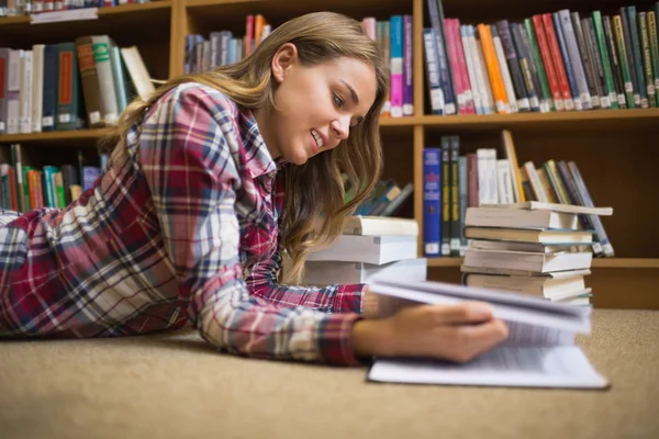 Улыбающийся студент лежит на полу библиотеки и читает — стоковое фото