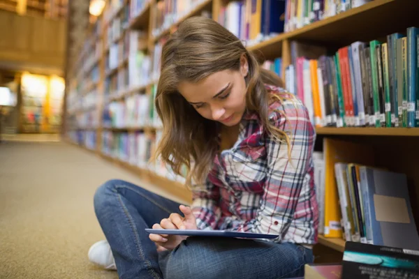 Pretty student sitting on library floor using tablet Stock Photo