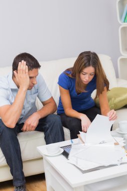 Worried couple paying their bills in living room at home clipart