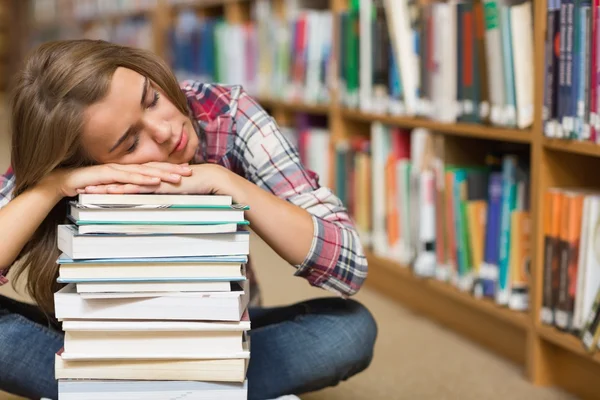 Estudante adormecido sentado no chão da biblioteca apoiado em pilha de livros — Fotografia de Stock