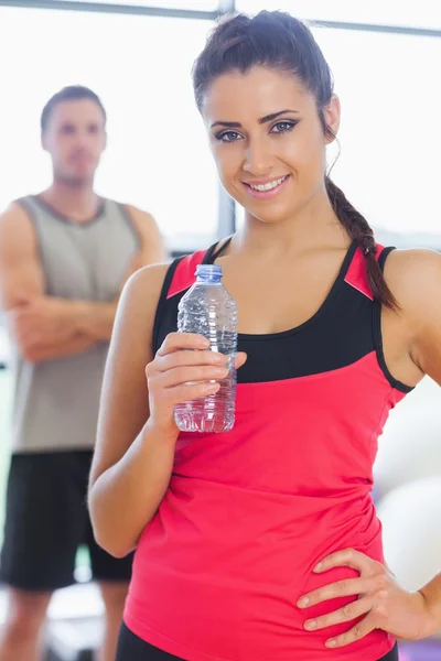 Fitte Frau mit Wasserflasche im Hintergrund im Fitnessraum — Stockfoto