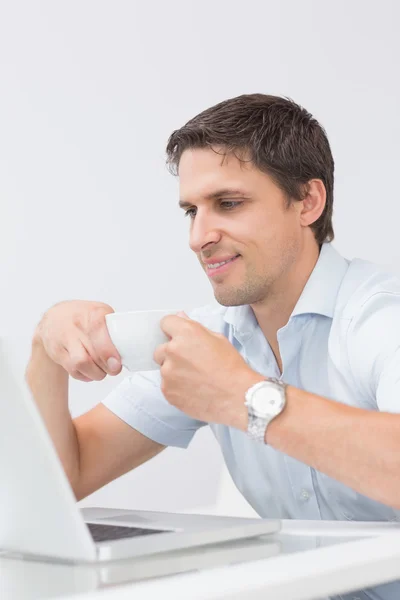 Çay fincanı dizüstü evde kullanma ile gülümseyen genç adam — Stok fotoğraf