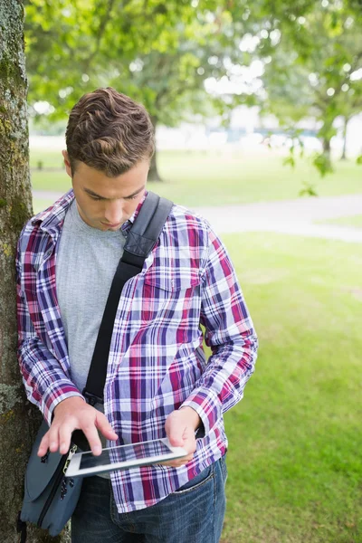 Estudiante guapo apoyado en el árbol usando su tableta — Foto de Stock