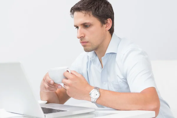 Allvarlig man med tekopp med laptop hemma — Stockfoto