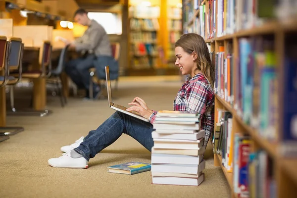 Uśmiechający się uczeń korzysta z laptopa na piętrze biblioteki — Zdjęcie stockowe