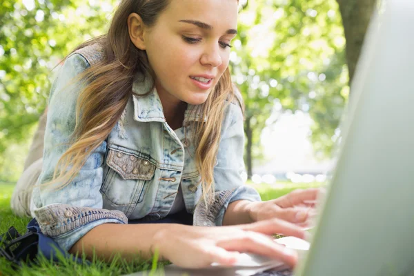 Junge glückliche Studentin liegt mit Laptop im Gras — Stockfoto