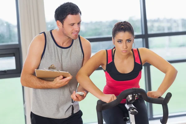 Trainer watching woman work out at spinning class — Stock Photo, Image