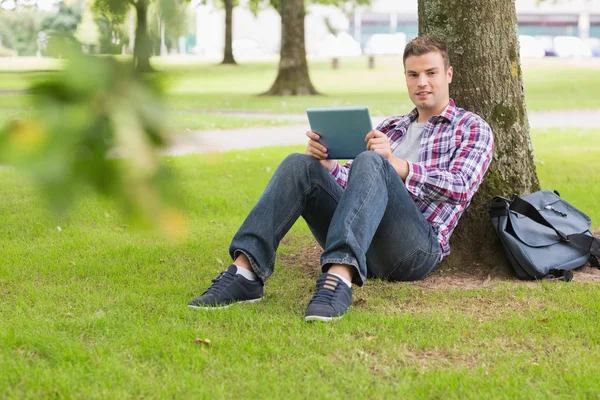 Feliz estudiante utilizando su PC tableta fuera apoyado en el árbol —  Fotos de Stock
