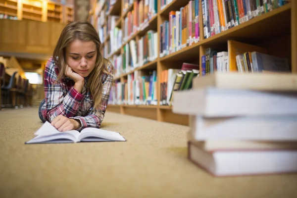 Ganska fokuserad elev liggande på biblioteket golvet läser bok — Stockfoto