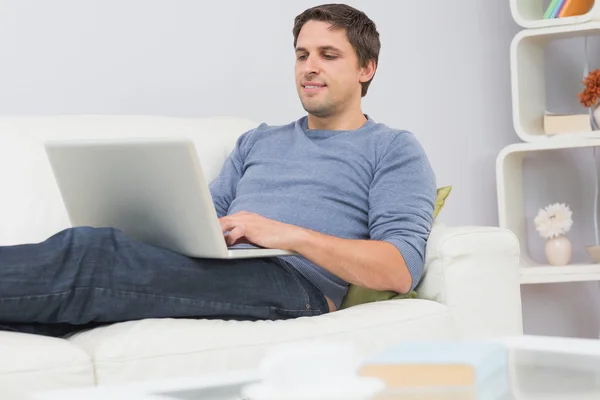 Relaxado jovem usando laptop na sala de estar — Fotografia de Stock