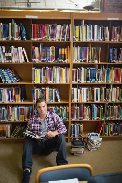 Handsome young student sitting on library floor reading book — Stock Photo, Image