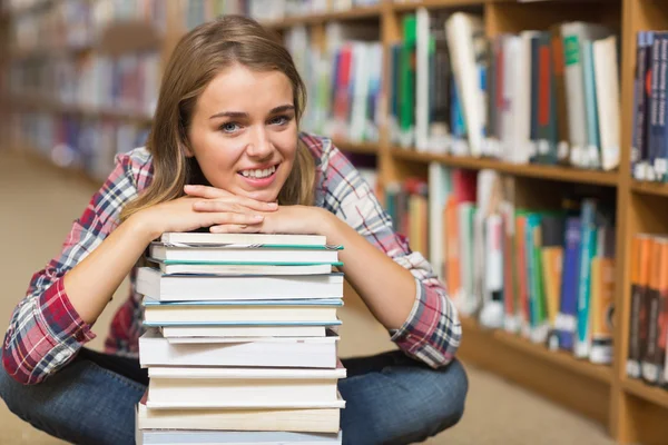 Uśmiechający się uczeń siedział na piętrze biblioteki, opierając się na stos książek — Zdjęcie stockowe