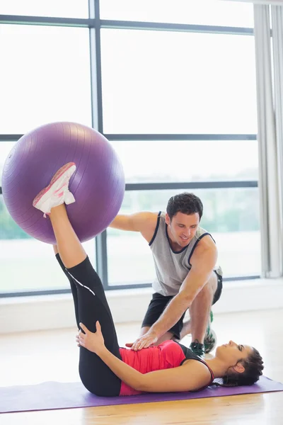 Školitel pomáhá mladá žena s fitness míč v tělocvičně — Stock fotografie