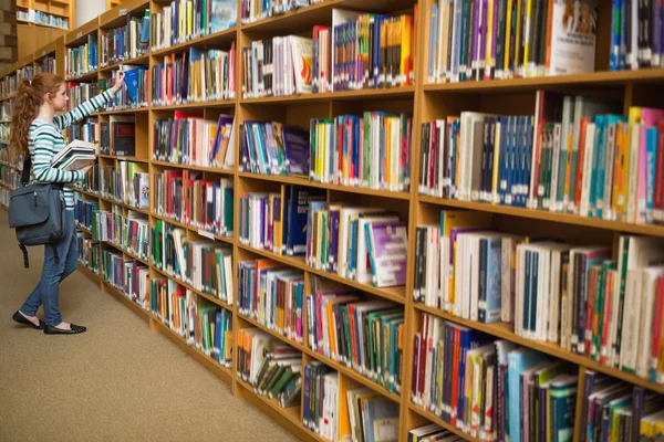 Rödhårig student med en bok från biblioteket bokhylla — Stockfoto