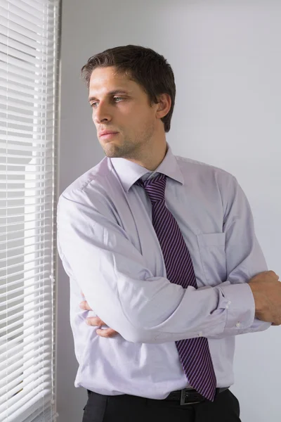 Serious businessman peeking through blinds in office — Stock Photo, Image